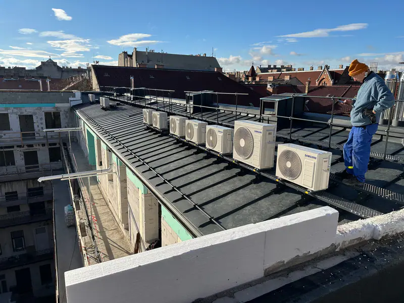 Kültéri klímaegységek sora egy társasház tetején, mellettük a szerelőnk